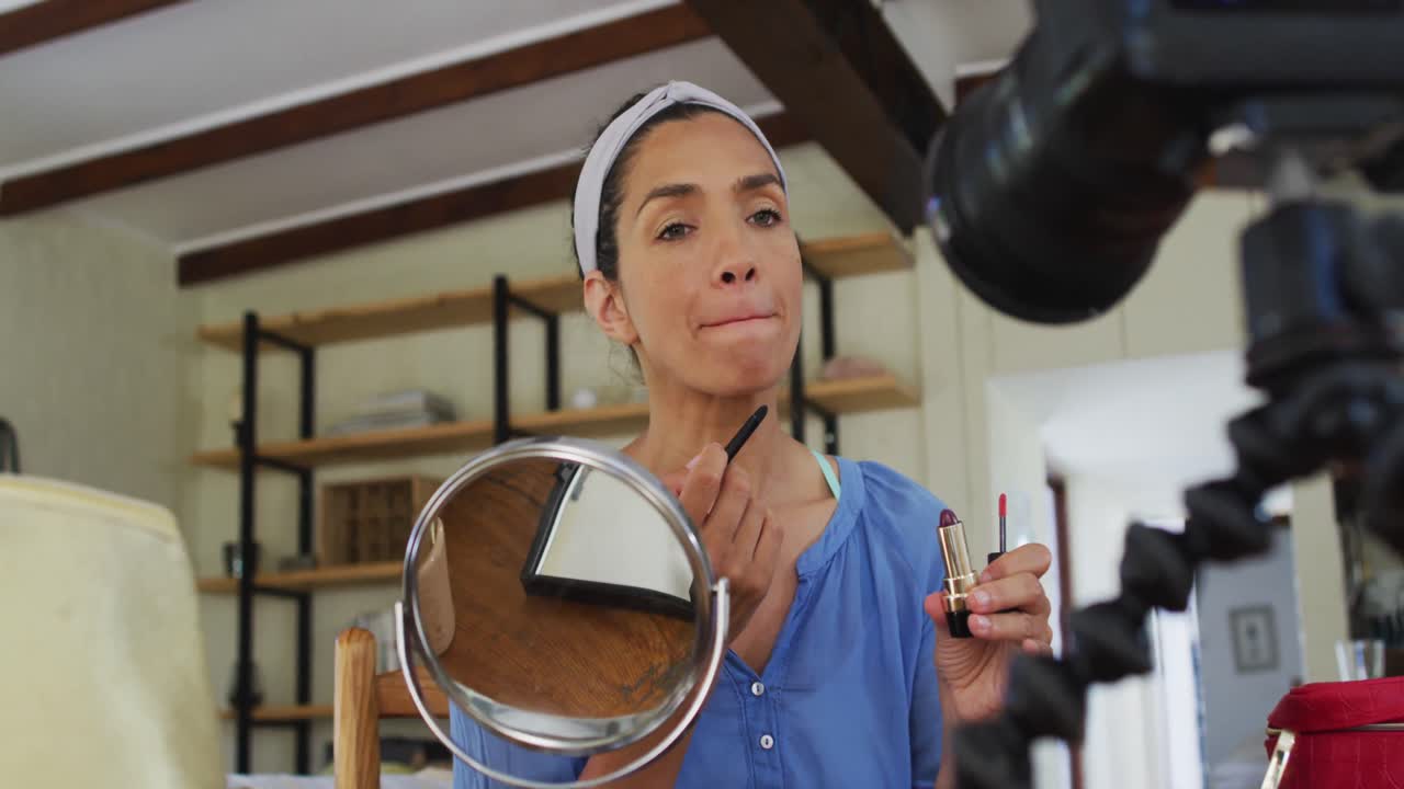 vlogger femenina de raza mixta aplicando maquillaje y grabando en cámara digital en casa