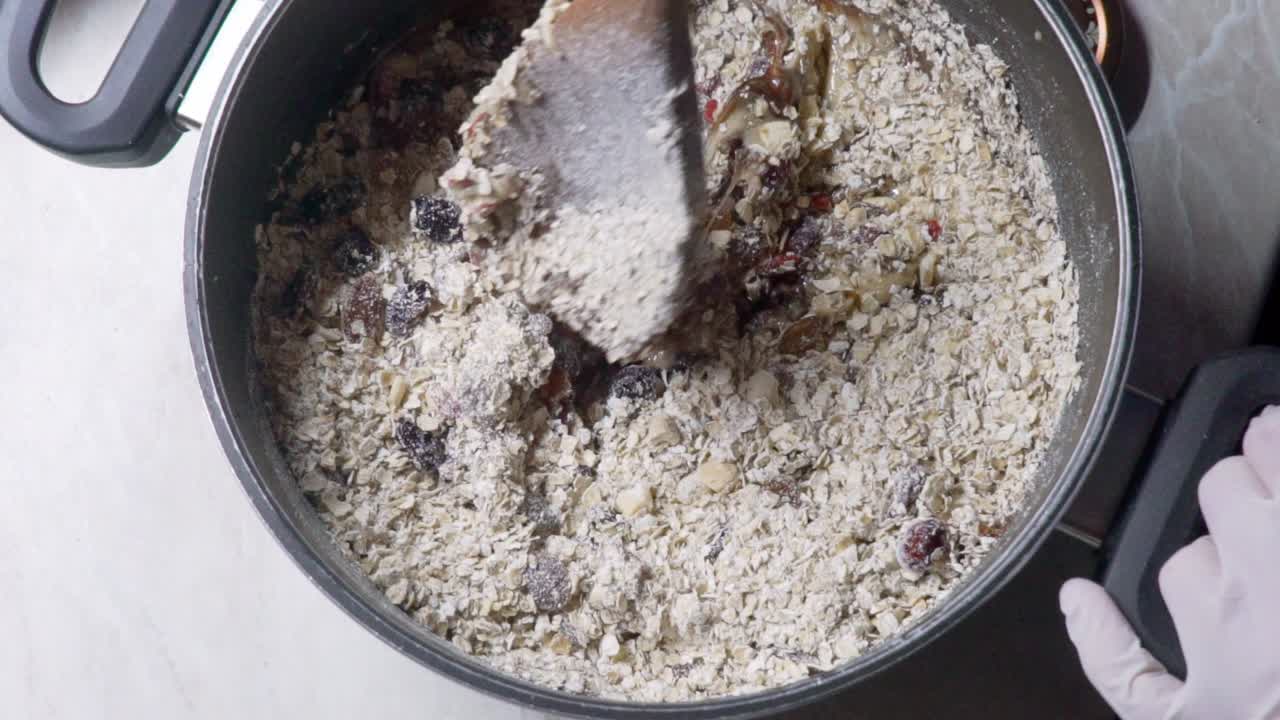 vista de pájaro de una mujer con guantes de látex de un solo uso, mezclando barras de energía caseras, usando una cuchara de madera, cámara lenta 120 fps