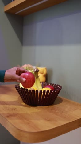 person reaching for an apple in a fruit bowl