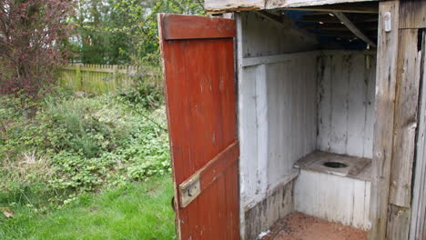 old wooden outhouse toilet with open door, displaying rustic toilet, set in a green rural setting