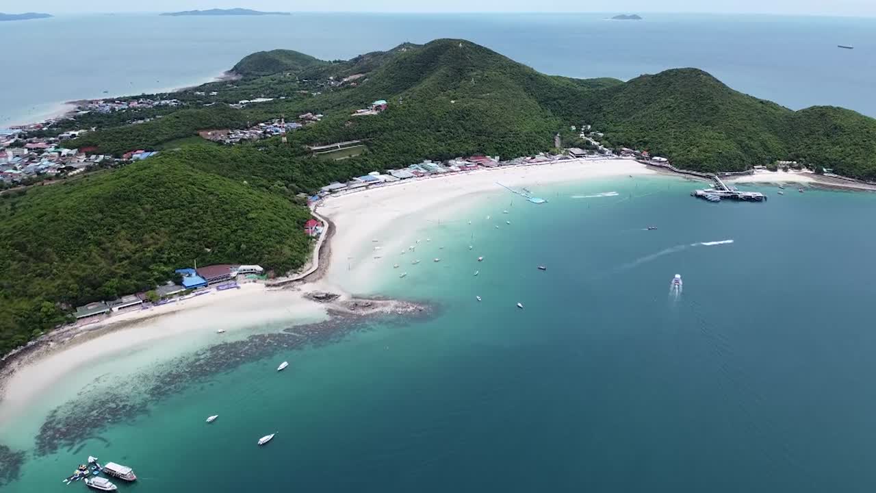Drone video captures Chaweng Bay's turquoise waters, boats, and resorts bordered by lush hills. The overhead shot highlights vibrant tourism, tropical tranquility, and bright daylight