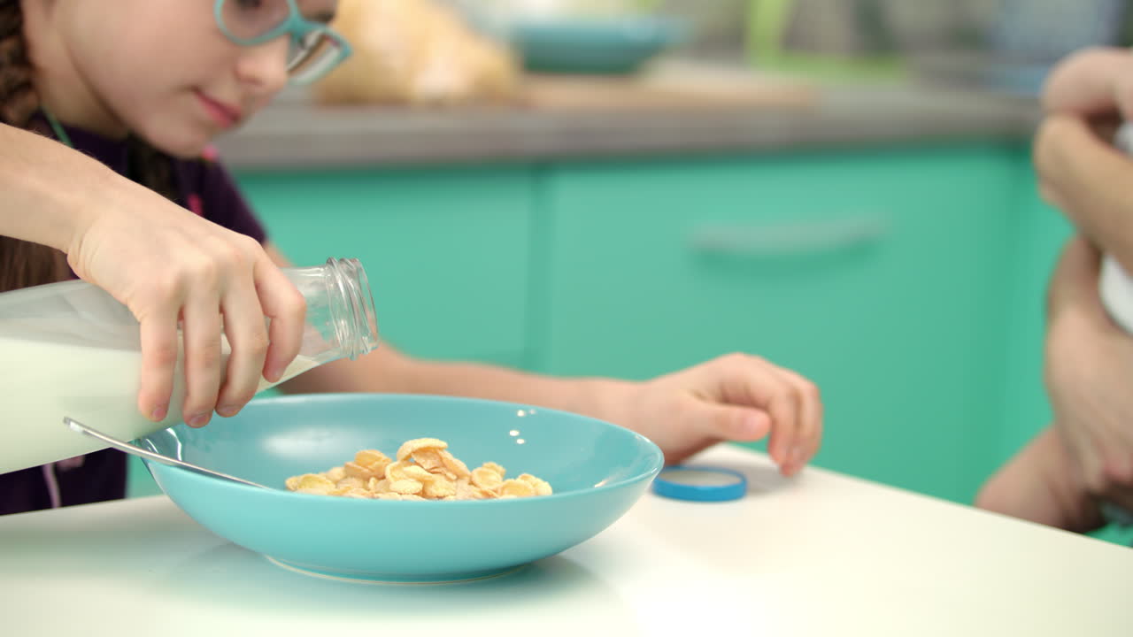 chica vertiendo leche en un tazón de vidrio de copos de maíz. estilo de vida saludable