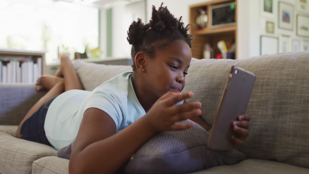 Happy african american girl lying on sofa using tablet