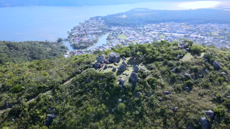 aerial drone scene of mountain with rocks on top with city between ocean and river in background