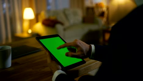 en casa, el hombre se sienta en su escritorio y usa una tableta con pantalla verde. su apartamento está hecho en colores amarillos y es cálido.