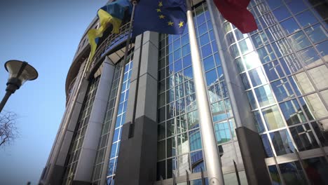 modern glass facade of the european parliament headquarters with waving international flags