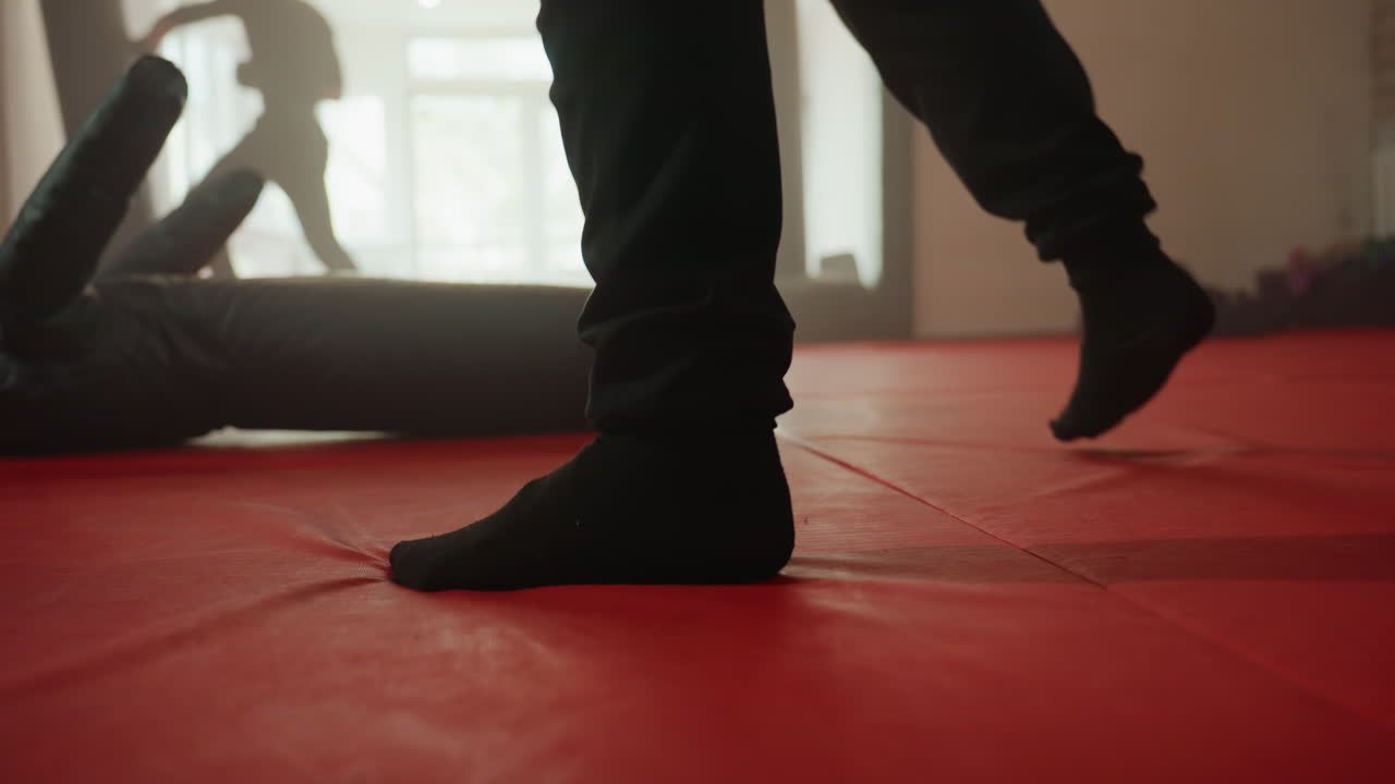 Boxer wearing black socks on red mat in gym during training session, legs tense with focus, background showing sparring activity, combat readiness, strength, discipline, and athletic determination