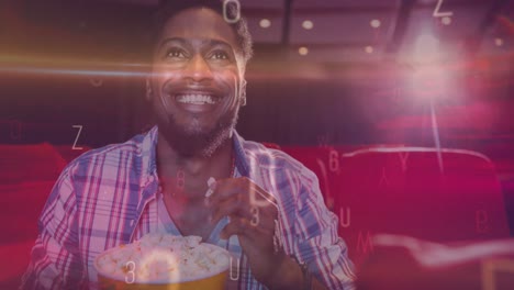animation of letters over smiling african american man eating popcorn in cinema