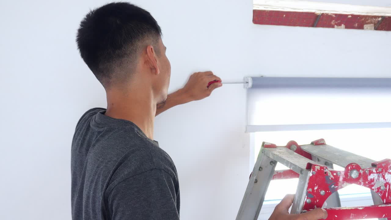 Handyman expertly installing modern roller blinds with precision using screwdriver on stepladder