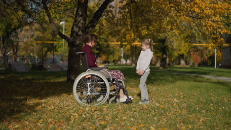 mother in wheelchair and daughter communicate in park