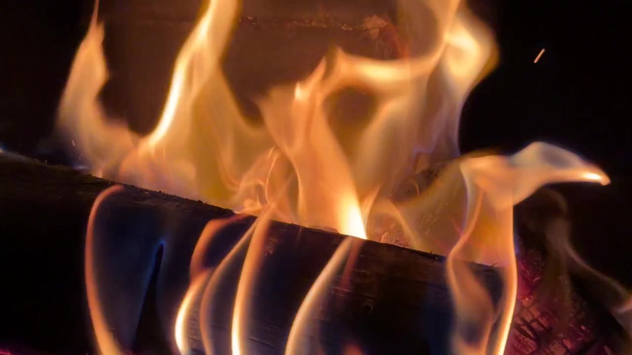 Orange flammer flimrer over forkullede brændestykker i en mørk pejs og skaber en varm, hyggelig atmosfære.