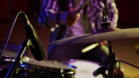 man with dreadlocks playing drums in a music studio