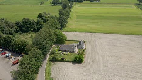 aerial of small farm house near a harvested pasture surrounded by green meadows