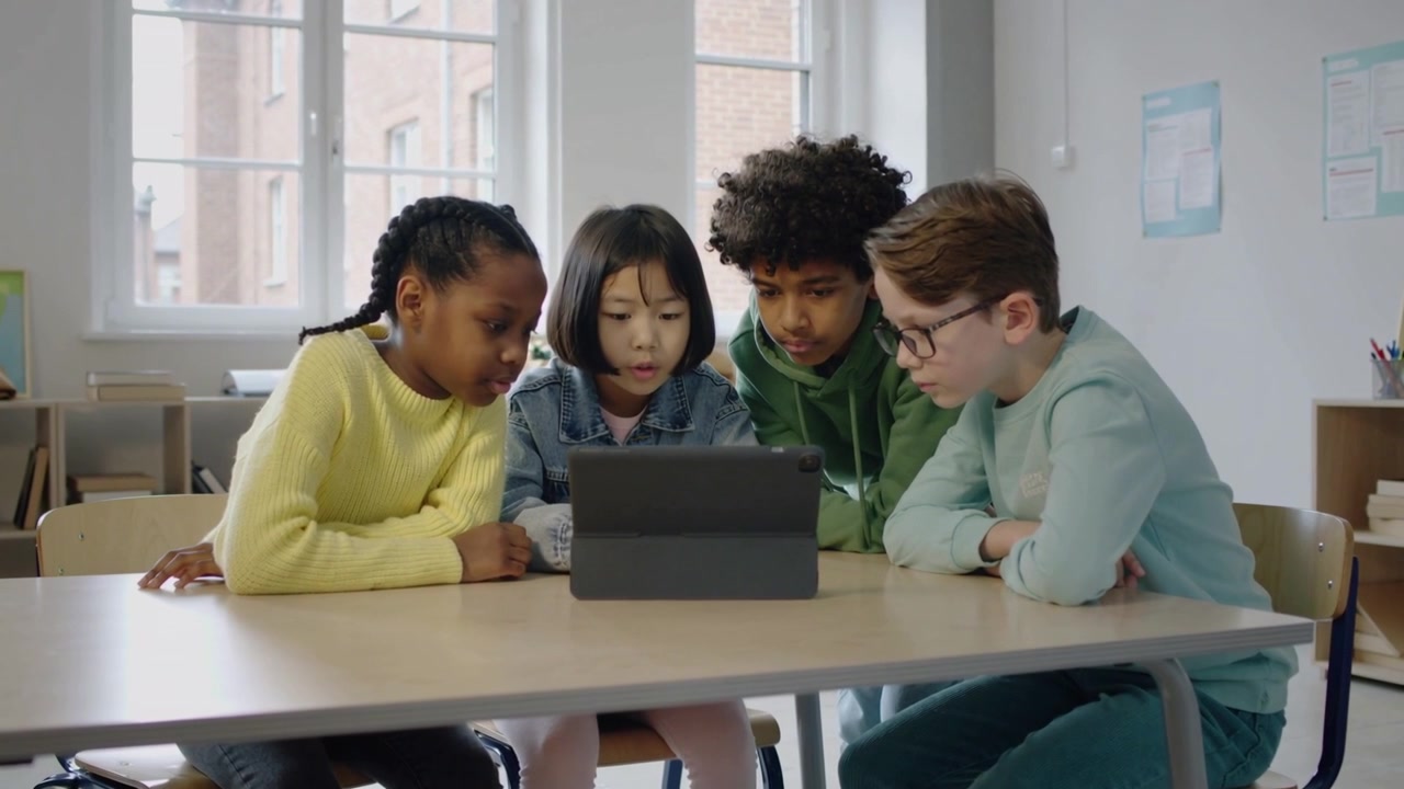 Leaning four students watching tablet after lesson starts on tablet at school table, folio case
