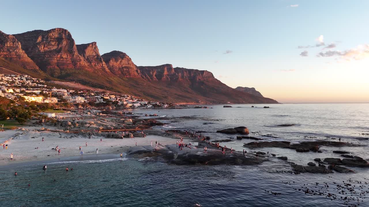 sunset aerial view of Cape Town South Africa drone fly above Atlantic Ocean during golden hours, tourist swimming with scenic mountains in background travel holiday destination