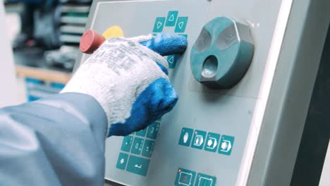 trabajador con guantes que controla una máquina industrial presionando botones de membrana