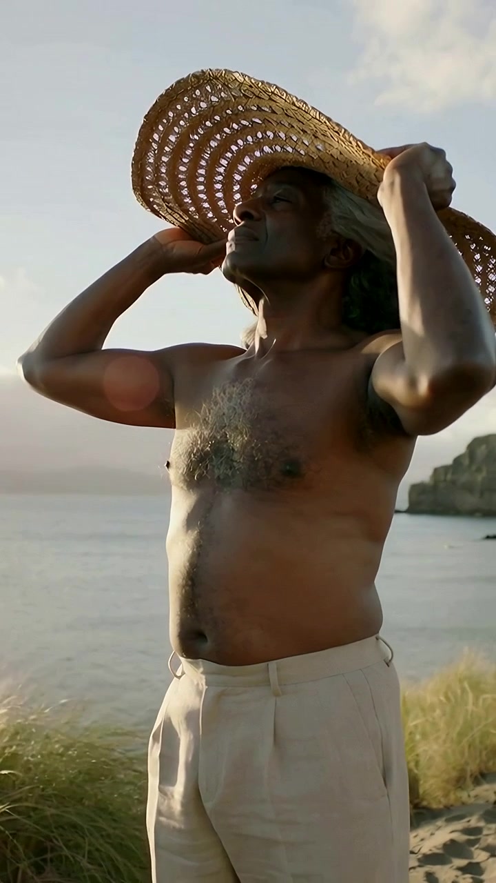 Video verticale: Anziano a torso nudo che si mette un cappello di paglia intrecciato in testa su un promontorio, riparandosi dalla brezza.