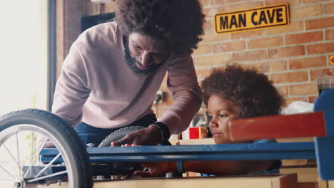 close up of pre teen son helping his father build him a racing kart, standing at a workbench in their garage, low angle, selective focus