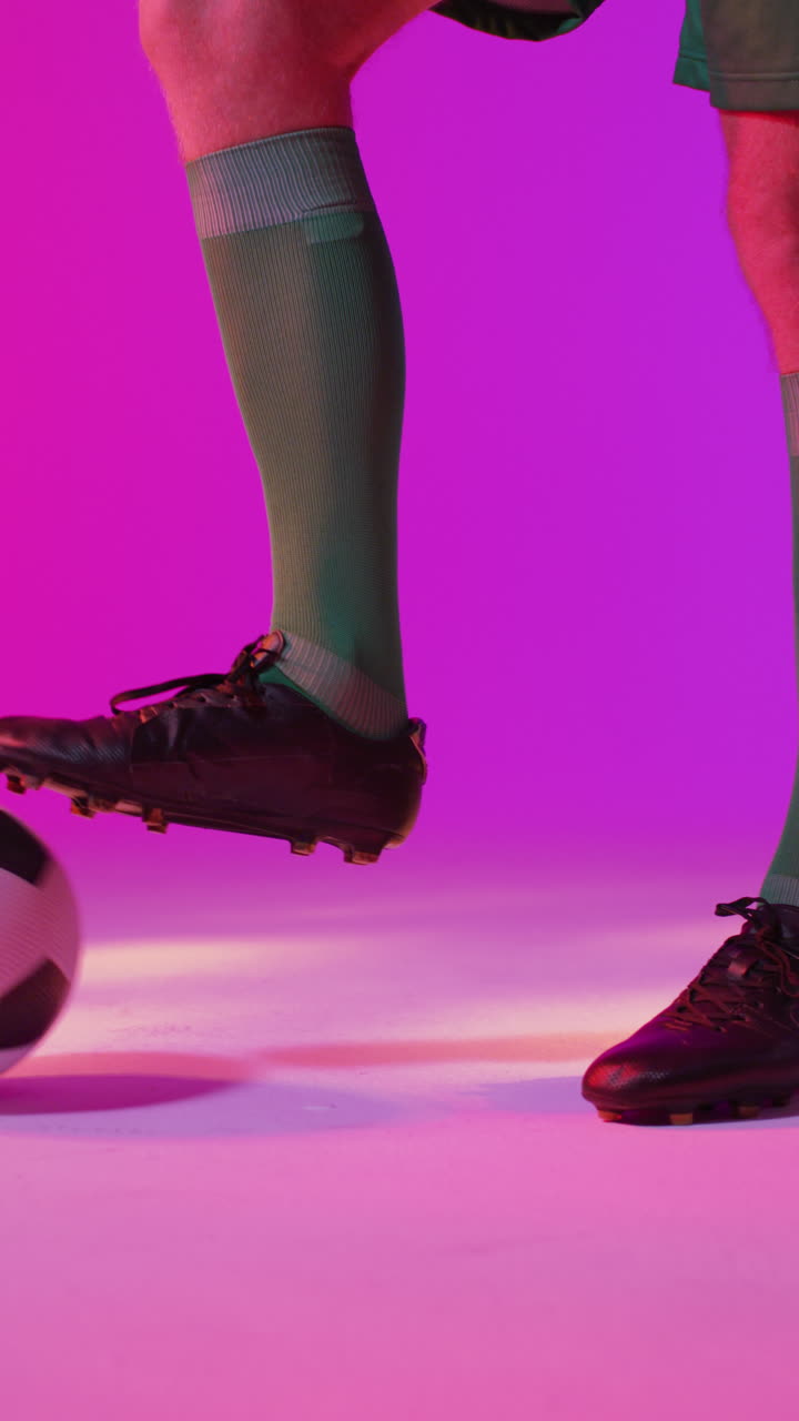 백인 남성 축구 선수 의 수직 비디오 는 네온 분홍색 조명 위 에 축구 를 들고 있다