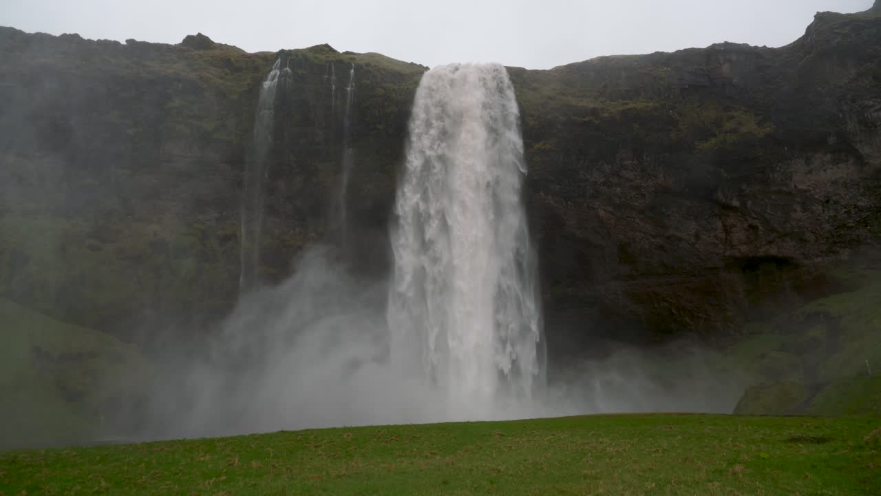 Water flooding over the edge of Seljalandsfoss waterfall in Iceland during a rainy time of year causes some flooding of the river below and produces a misty cloud for hikers