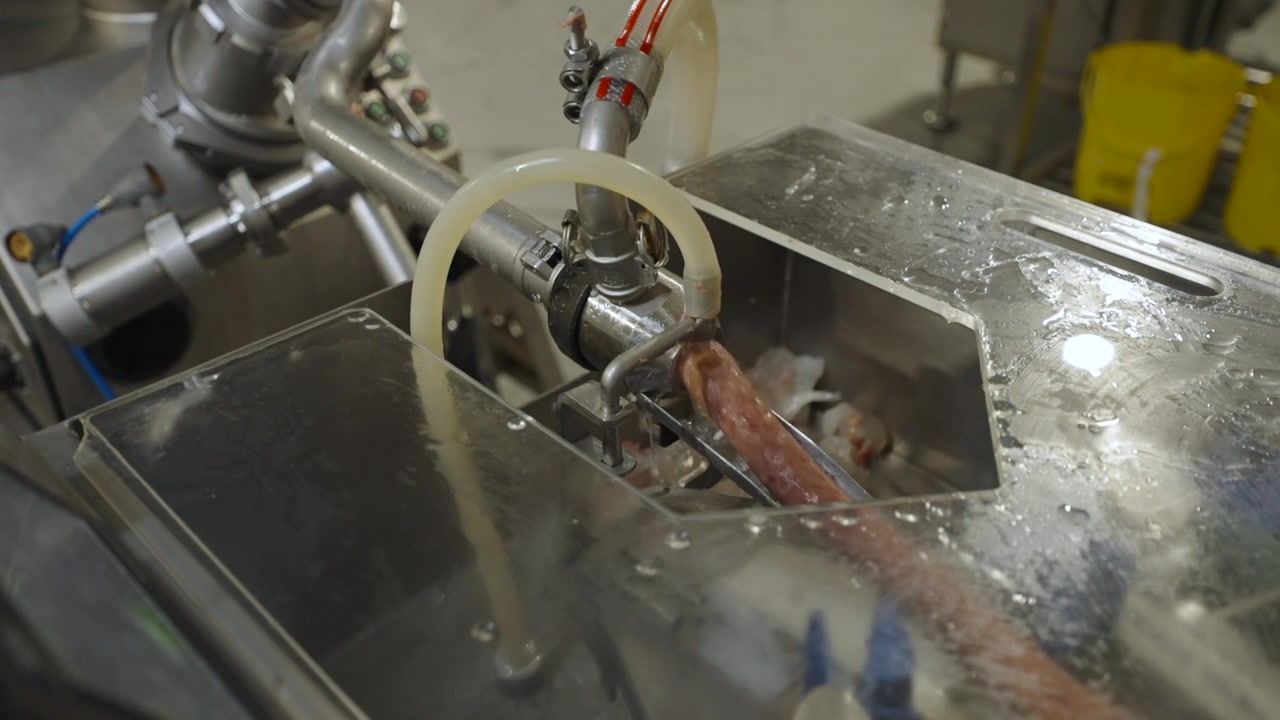 Alginate casing machine extrudes a continuous sausage strand across a wet stainless steel production line in a meat plant.
