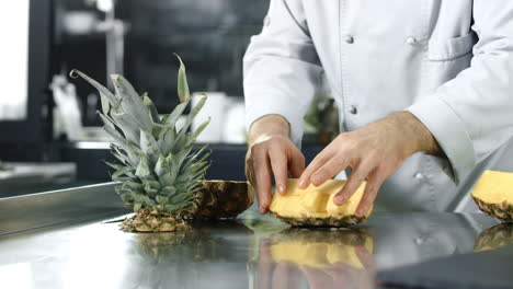 chef cutting pineapple at kitchen. closeup chef hands chopping healthy fruit.