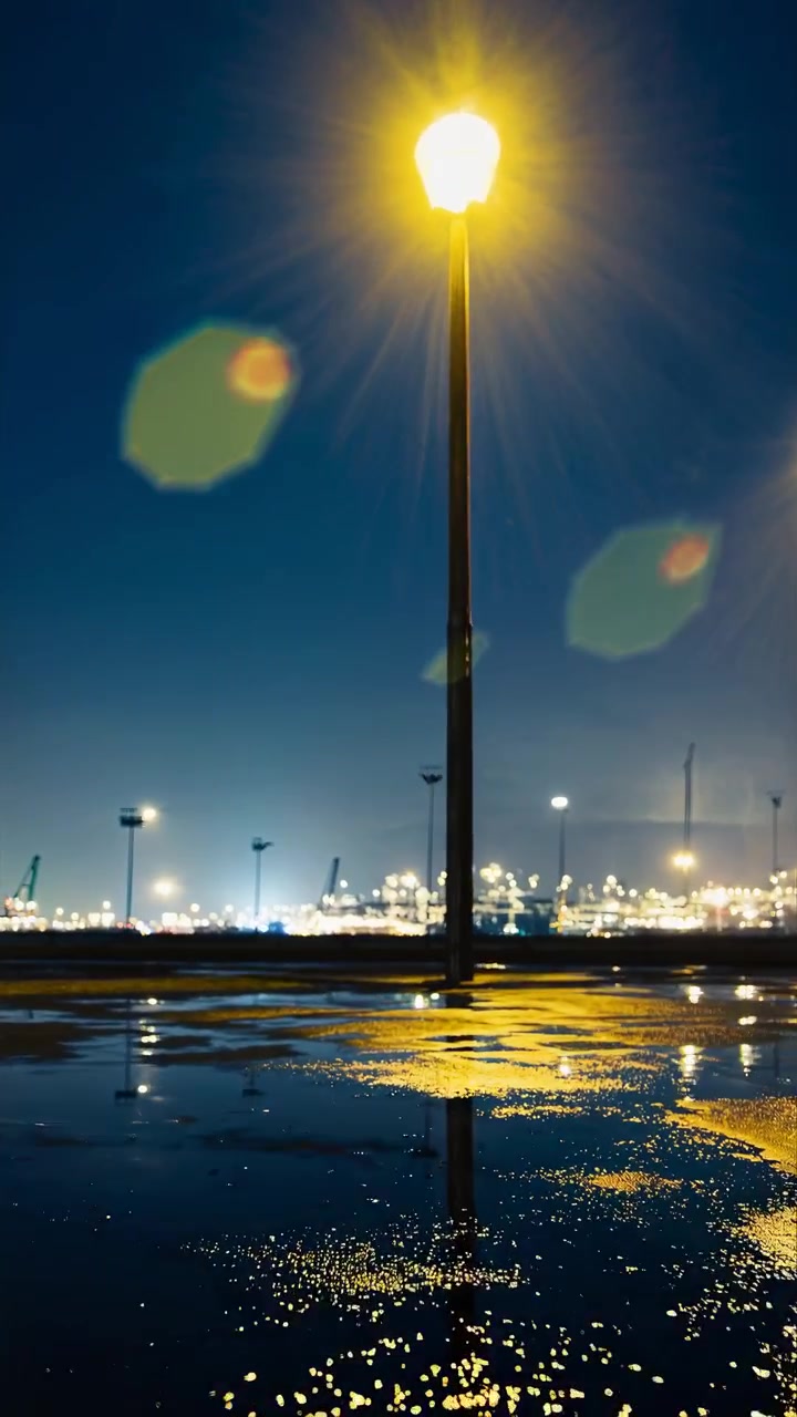 Farola reflejándose en un charco de noche cerca de un puerto industrial