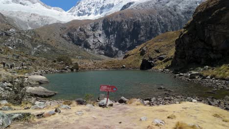 a dramatic aerial tilt up reveals the vivid turquoise laguna 69 framed by steep cliffs, rising to the snow-capped summit of chacraraju in peru’s cordillera blanca