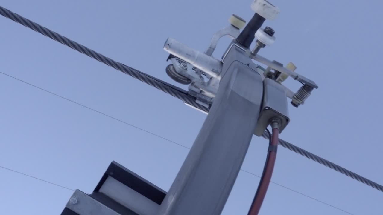una góndola pasa sobre un poste de soporte de metal, pequeñas ruedas de cable tiemblan, alpes suizos, saas fee, cielo azul