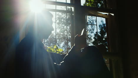 the young businessman in an abandoned house he sits on the windowsill uses a telephone silhouette in