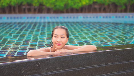 Una-Mujer-Sonriente-Se-Apoya-En-Sus-Manos-Y-Brazos-A-Lo-Largo-Del-Borde-De-La-Piscina-De-Un-Resort