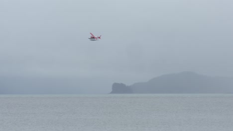 float plane flying over fjord in alaska on a foggy morning