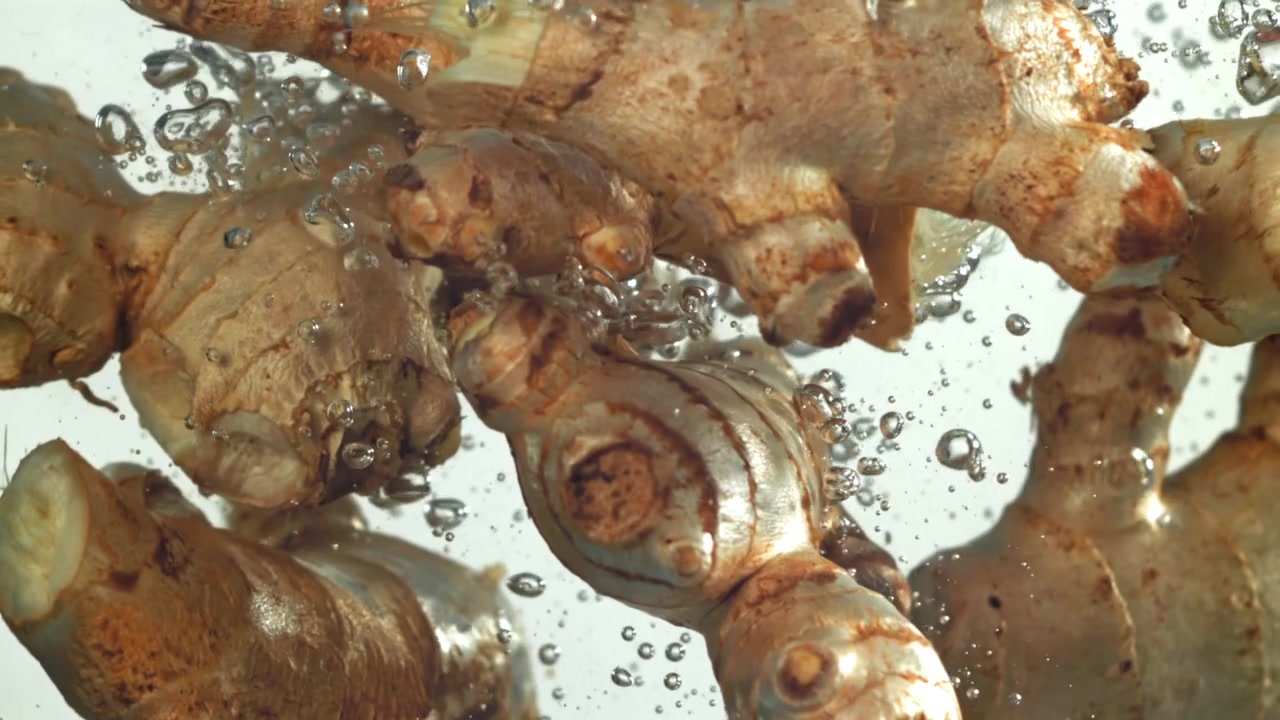 Fresh Ginger Roots Falling into Water with Bubbles in Slow Motion