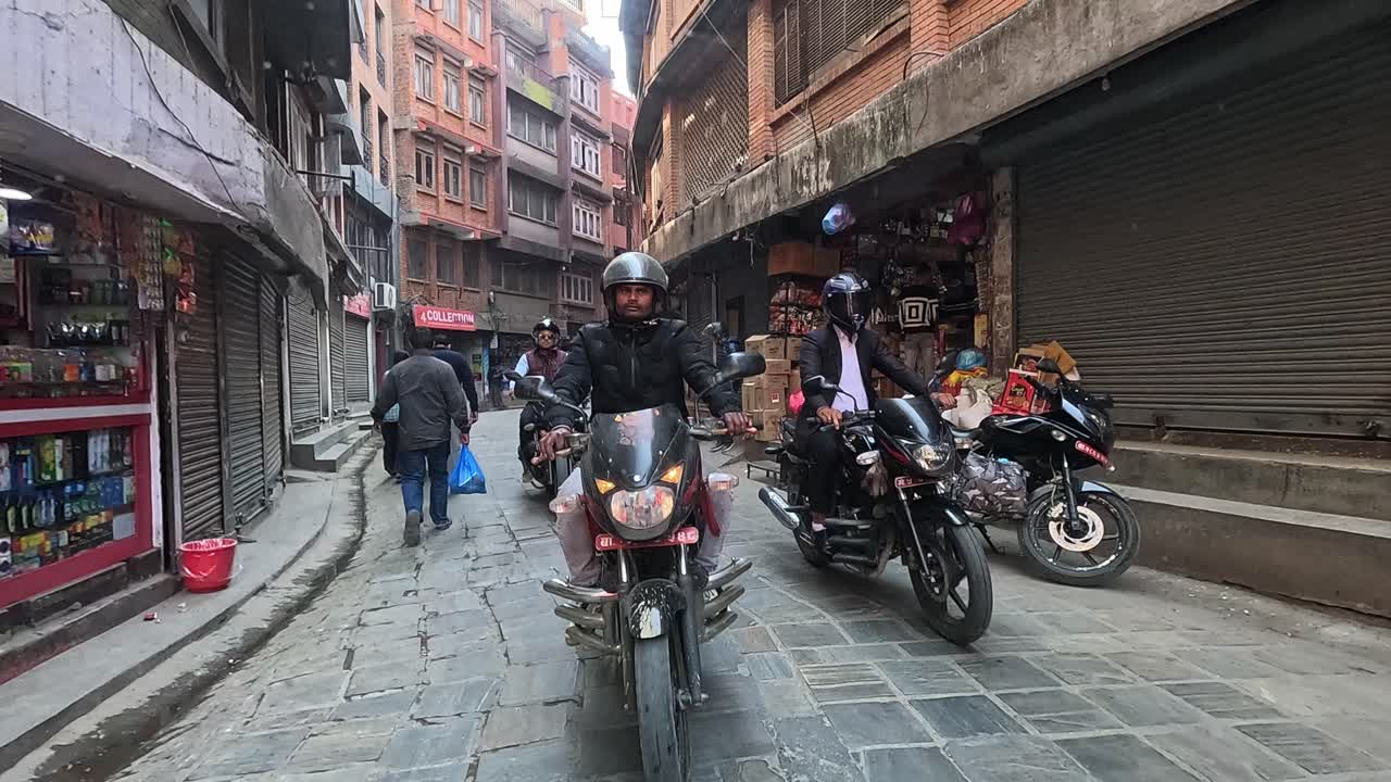 Backseat view of a car navigating the lively alleys of central Kathmandu, following motorbikers in a dynamic urban commute. Thamel area full of stores and narrow alleys