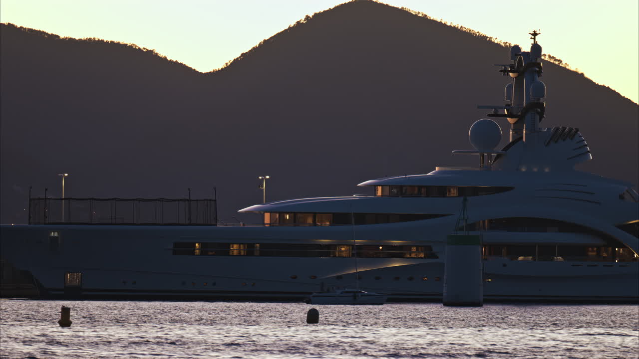 Boat moving on the sea, near a ship with the mountains on the background at sunset in Nice, France