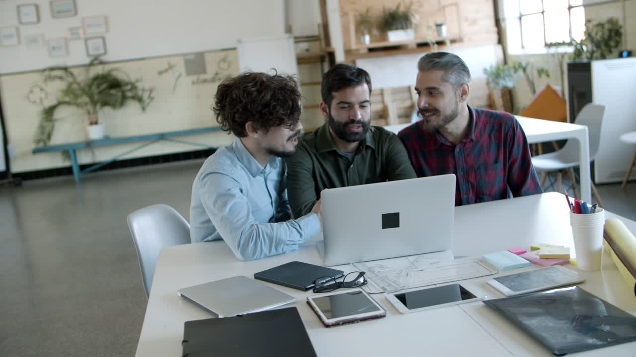 jóvenes enfocados hablando y mirando portátiles en una oficina acogedora