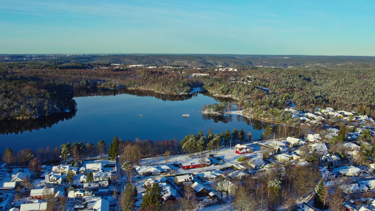 Luftaufnahme von schneebedeckten Häusern an einem Waldsee an einem klaren Wintertag