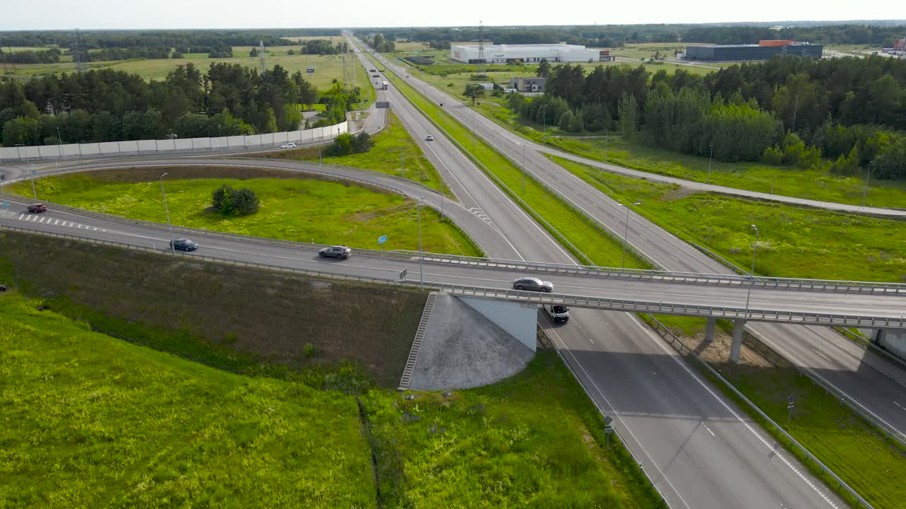 Aerial drone footage of a countryside sunny highway that is going under from a large intersection bridge during summer day with cars, vehicles, trucks and buses driving over and under it smoothly