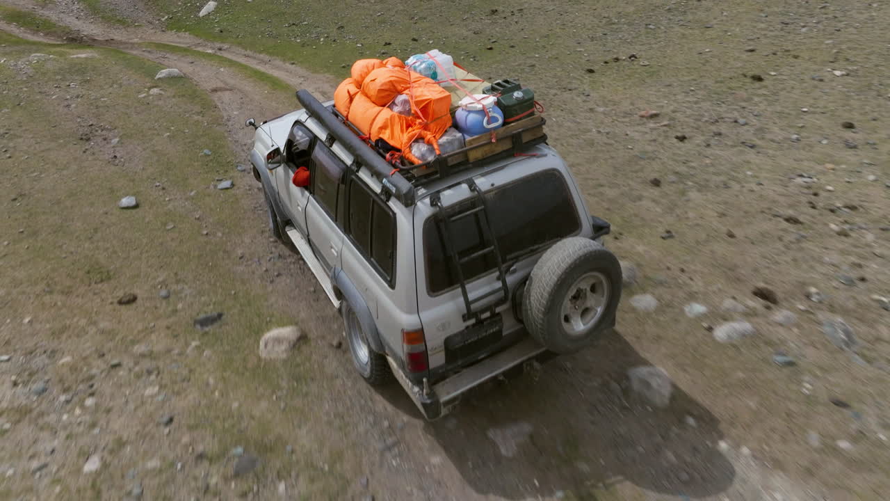 SUV che attraversa il terreno nella Valle di Tsagaan Gol, nelle Montagne dell'Altai in Mongolia. Ripresa aerea con tracking.