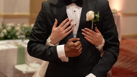 Groom-in-black-wedding-suit-with-his-hands-crossed-and-the-bride's-hands-hugging-each-other-from-behind-during-the-wedding-ceremony