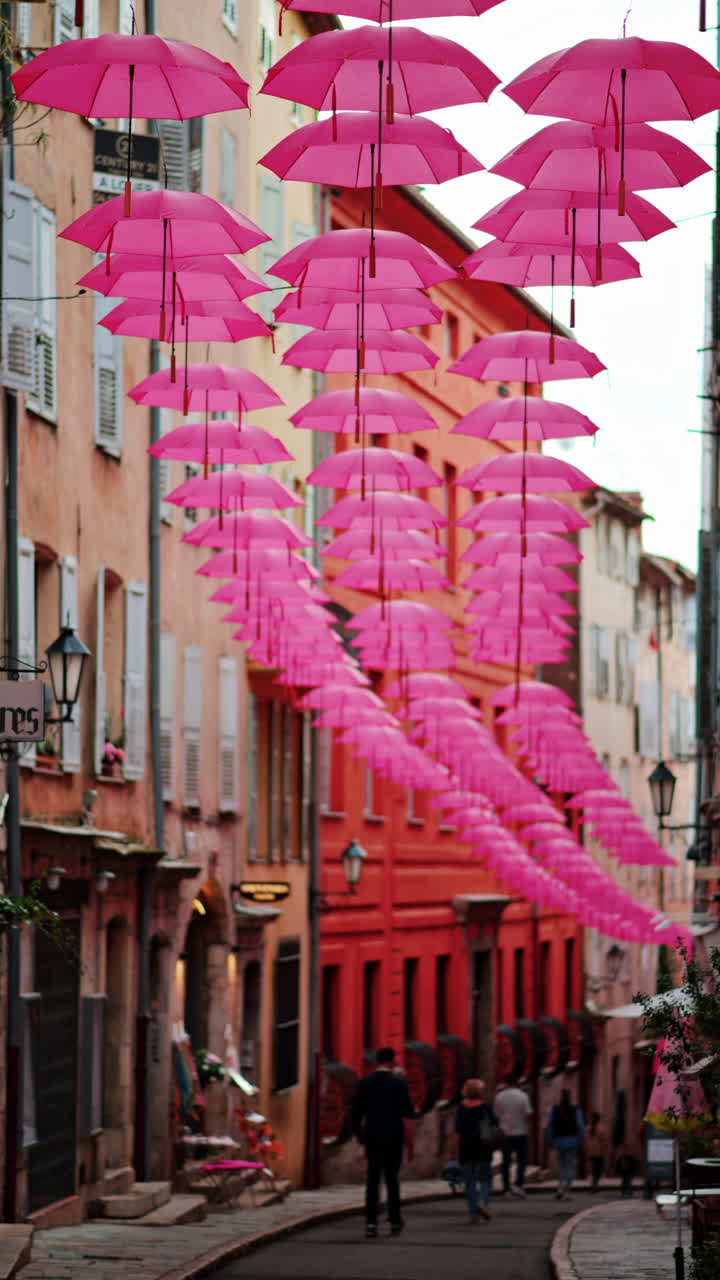 Rows of pink umbrellas above the streets of the old town in Grasse, France. Vertical