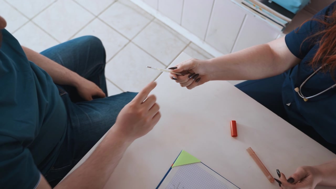 Verpleegkundige controleert temperatuur en vitale functies aan een kleine kliniektafel, thermometer uitgestrekt naar patiënt, stethoscoop zichtbaar, papierwerk en mappen op bureau, gerichte professionele omgeving met kalmte.