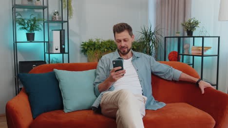 portrait of adult man sitting on sofa, using smartphone share messages on social media application