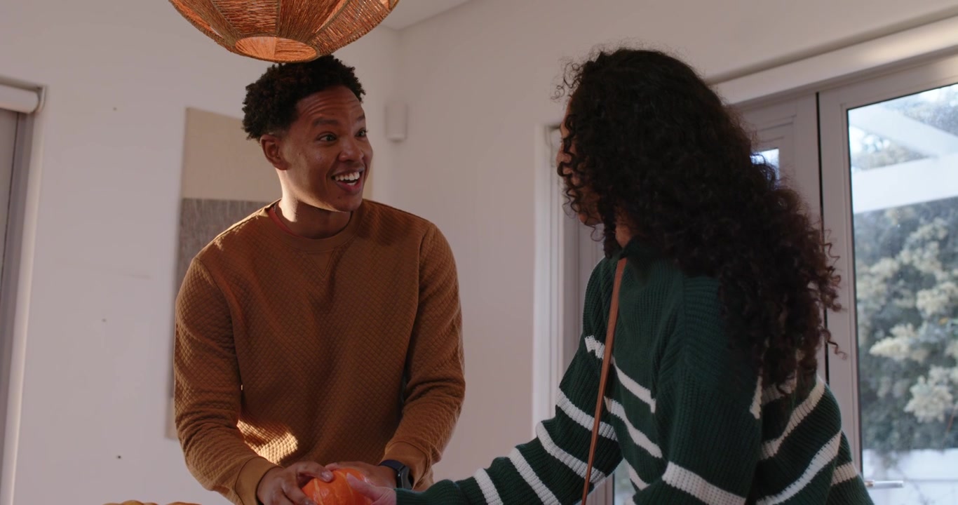 African American couple arranging pumpkins at table, woman removing mini pumpkin, man holding apple
