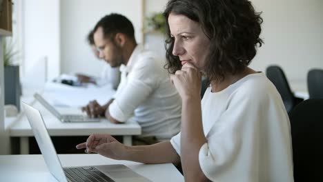 vista lateral de una mujer caucásica enfocada escribiendo en una computadora portátil