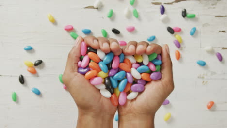 video of overhead view of biracial man holding multi coloured sweets over white rustic background