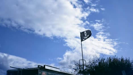 black pirate flag flutter on wind with partly overcast blue sky. jolly roger sign on building inland.