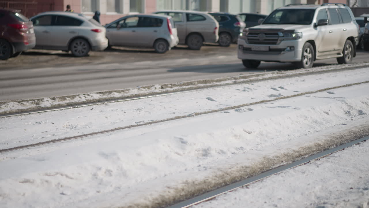 close view of tram train skirting past bus lane in winter city, metal wheels rolling on rail through snow, plow and undercarriage visible, urban public transport scene with signage, sunlight