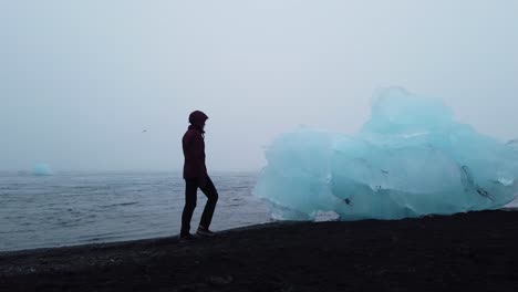 Turista-Caminando-En-La-Playa-De-Arena-Negra-Con-Icebergs---Breidamerkursandur-También-Conocida-Como-Playa-De-Diamantes-En-El-Sur-De-Islandia