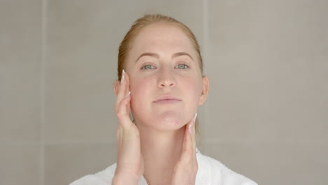 applying skincare, woman in bathrobe gently massaging face at home